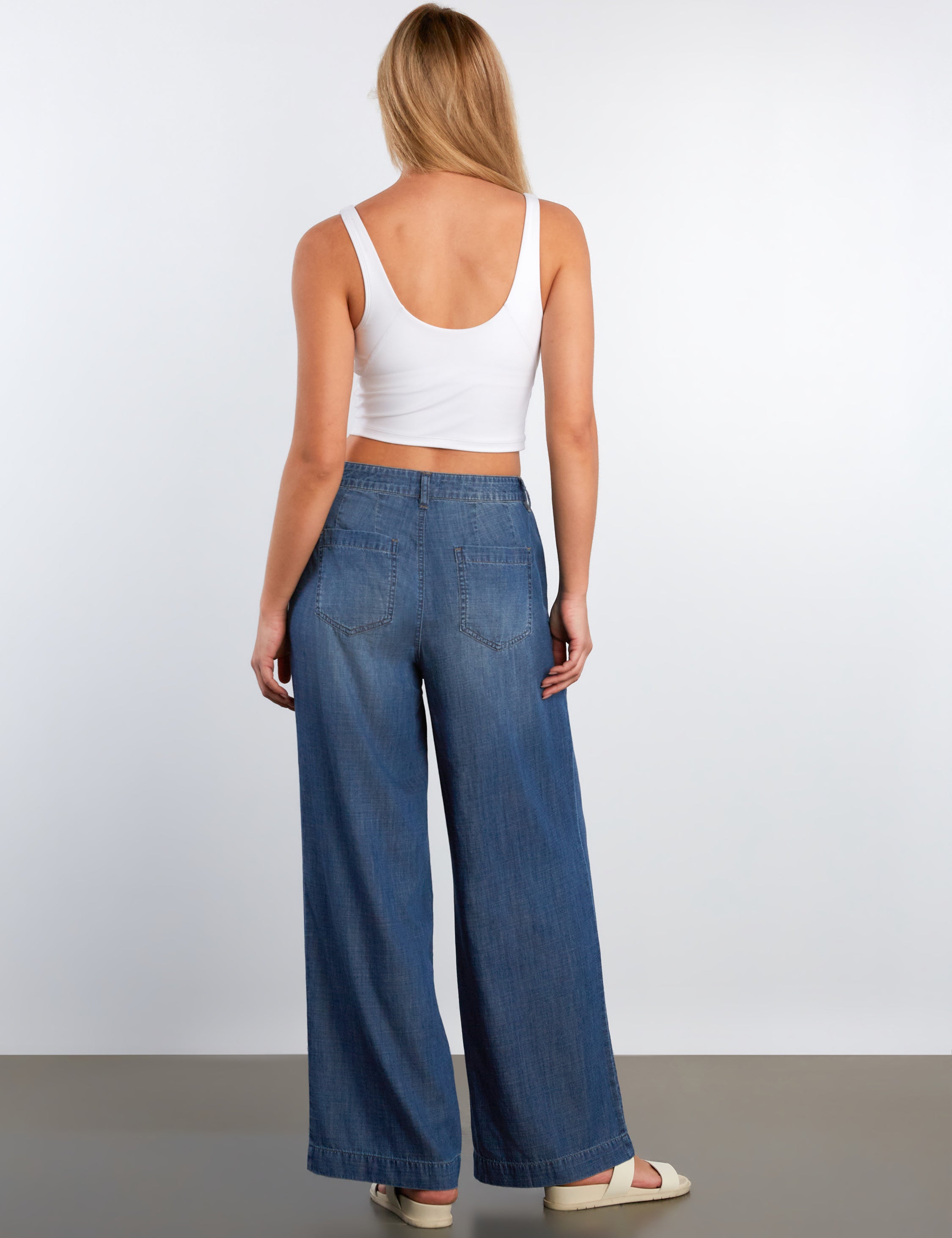 Woman wearing a white tank top and blue jeans against a plain background