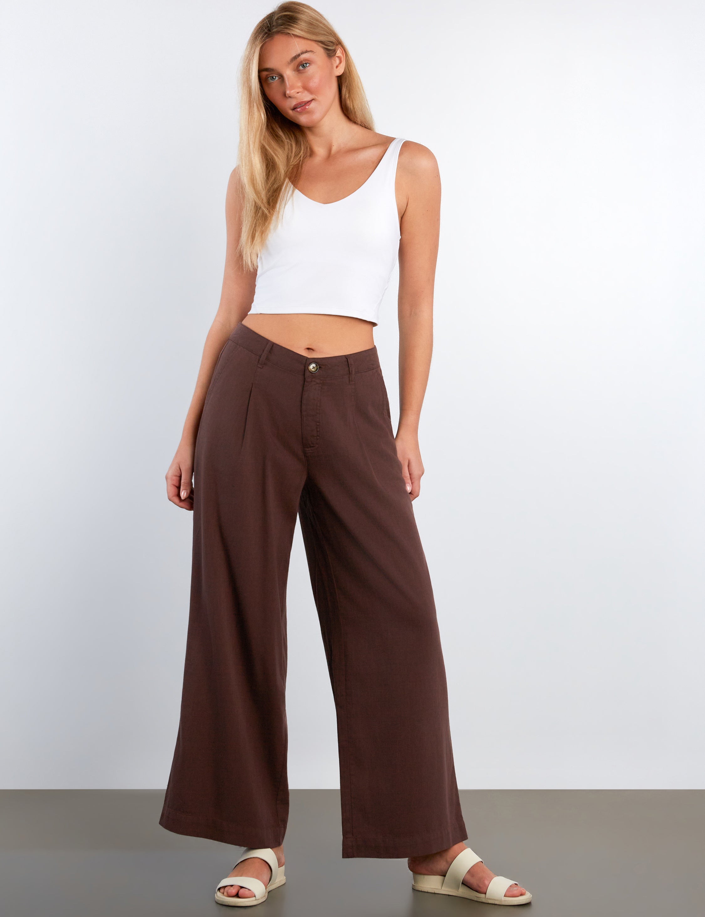 Woman wearing a white top and brown wide-leg pants against a white background