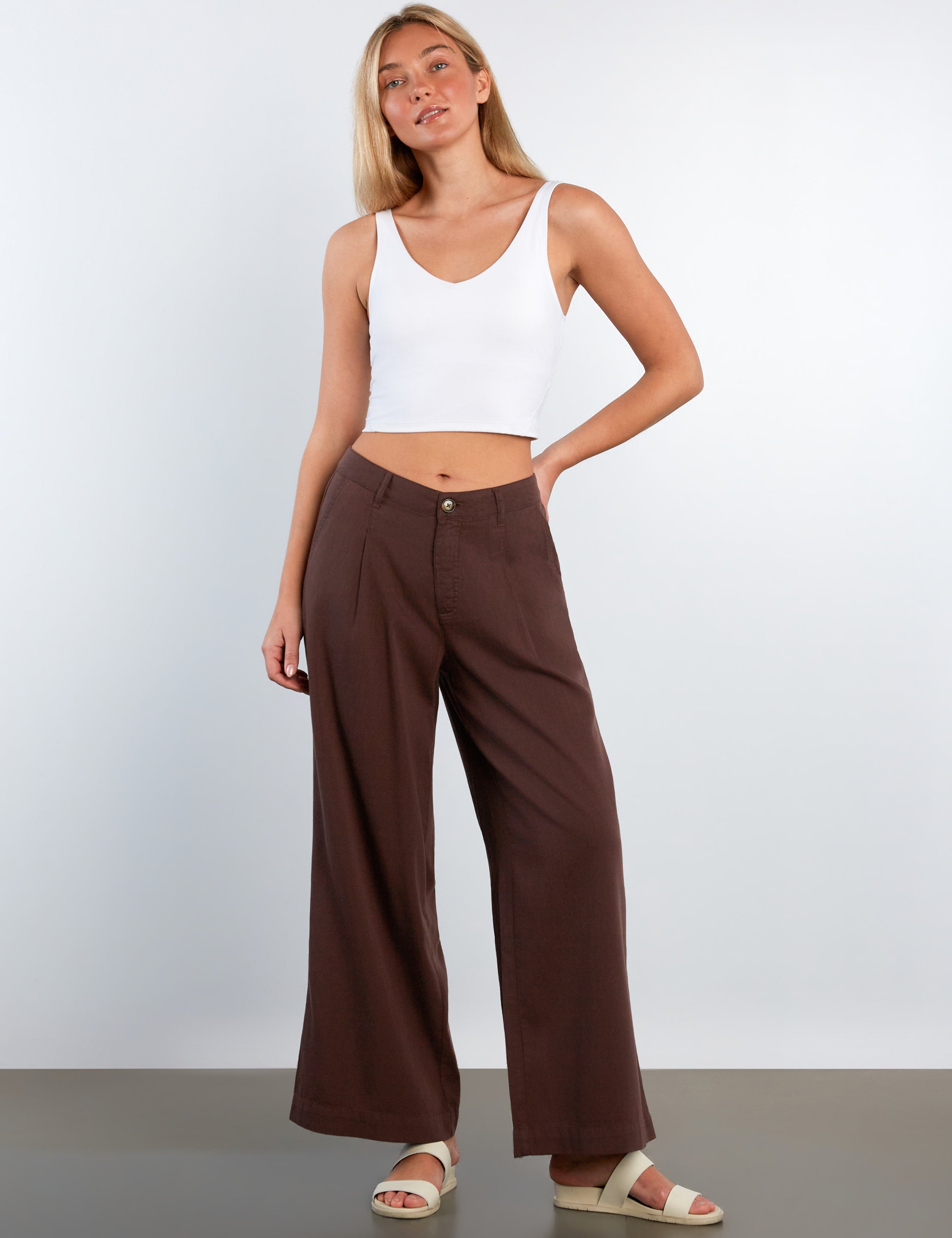 Woman wearing a white top and brown wide-leg pants against a plain background