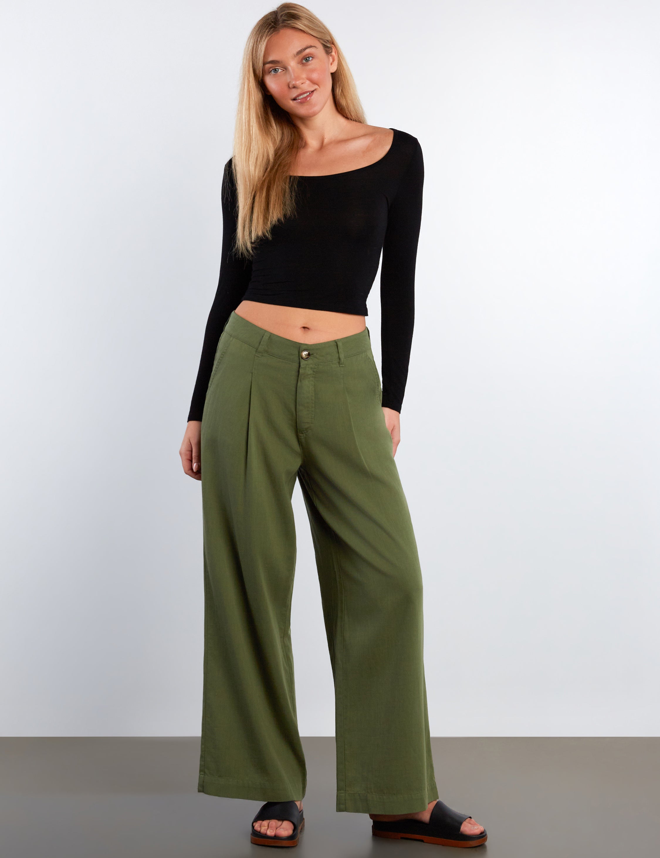 Woman wearing a black long-sleeve top and green wide-leg pants on a white background