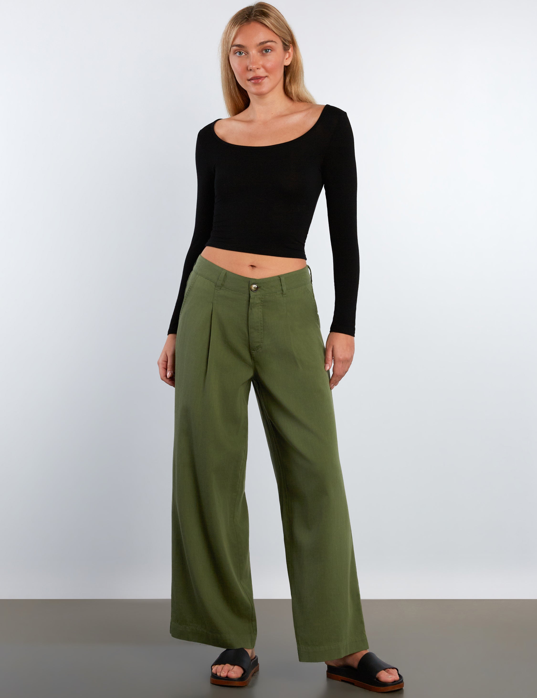 Woman wearing a black long-sleeve top and green wide-leg pants on a white background