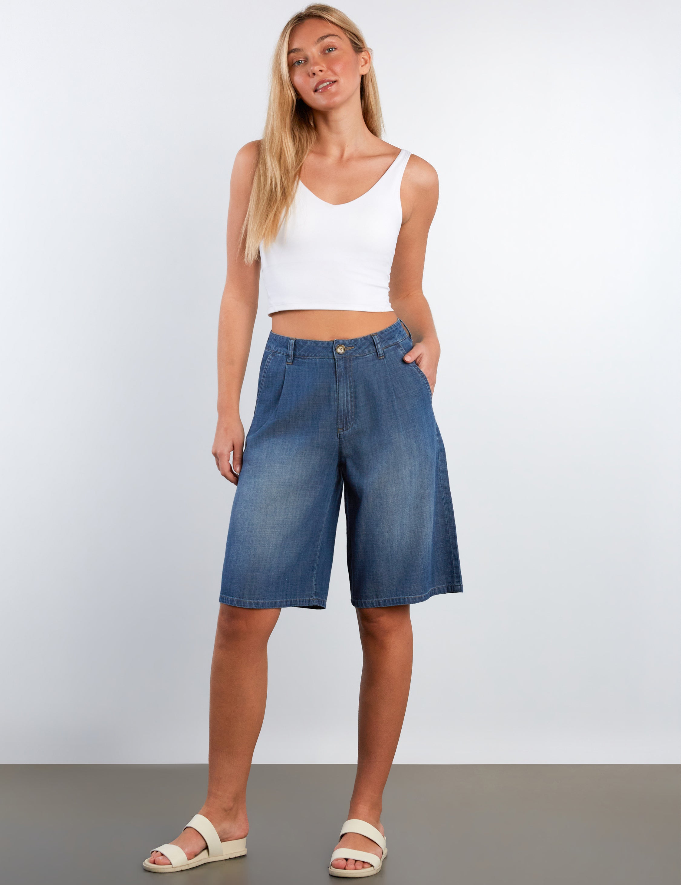 Woman wearing blue denim shorts and a white top on a plain background