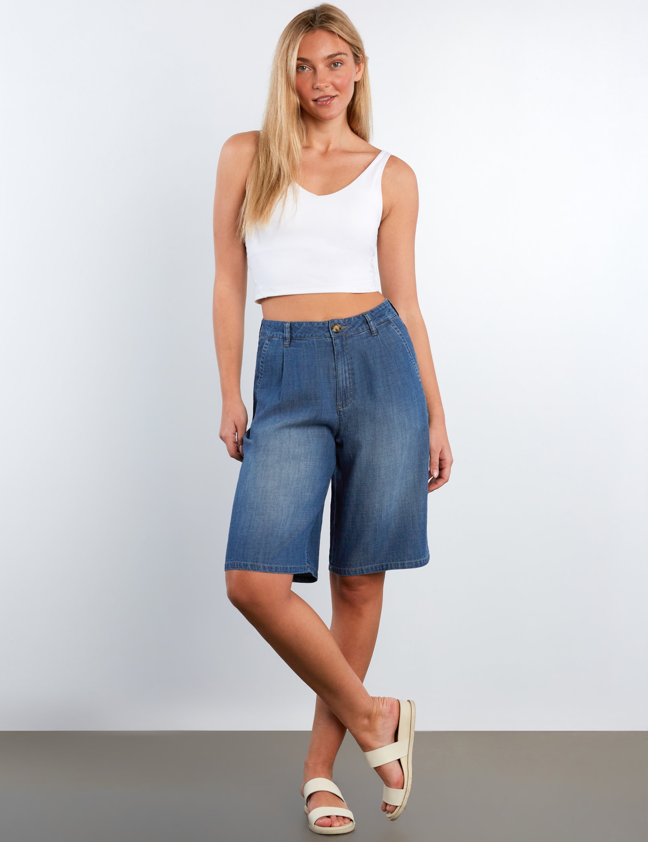Woman wearing blue denim shorts and a white top on a plain background