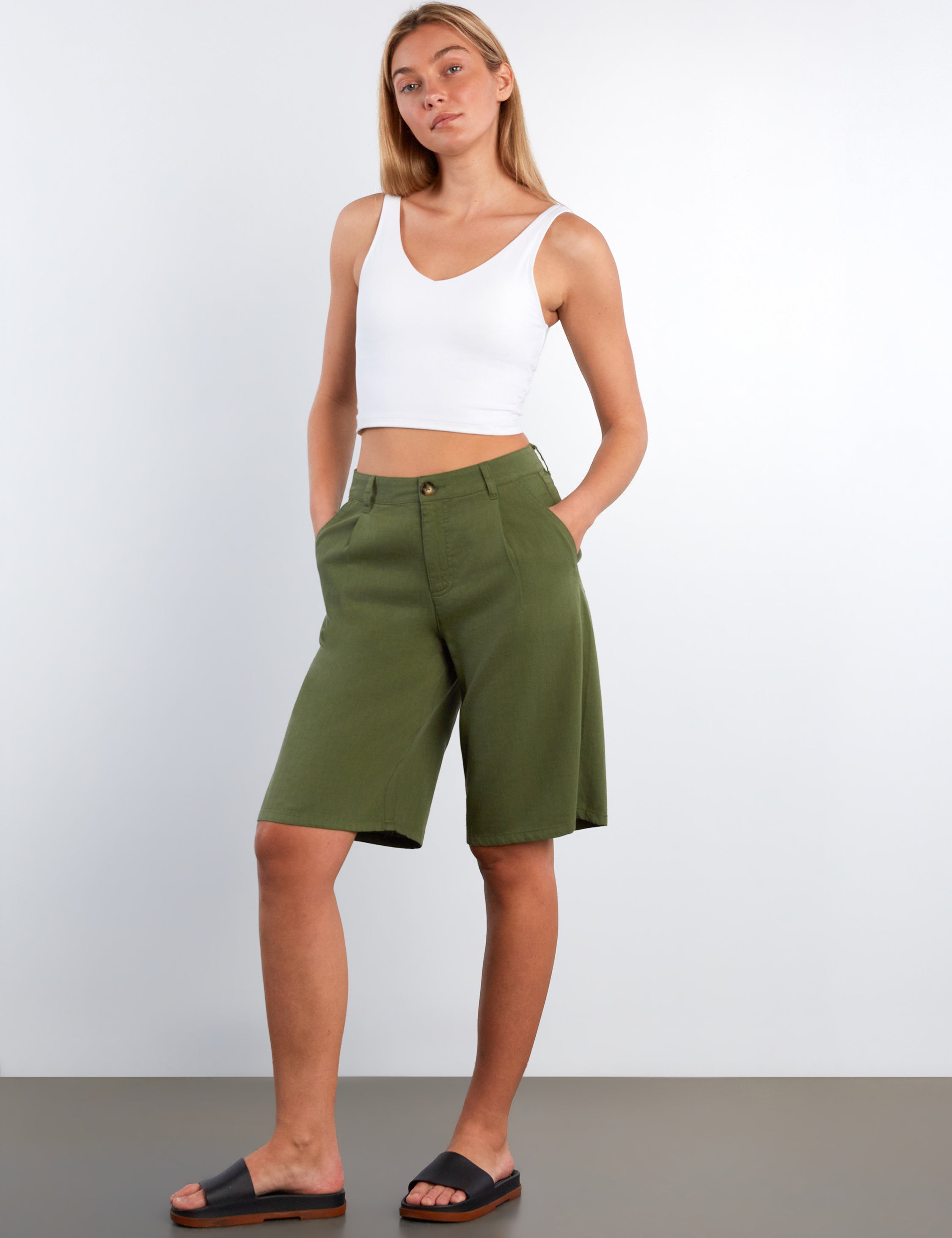 Woman wearing green shorts and a white top against a plain background