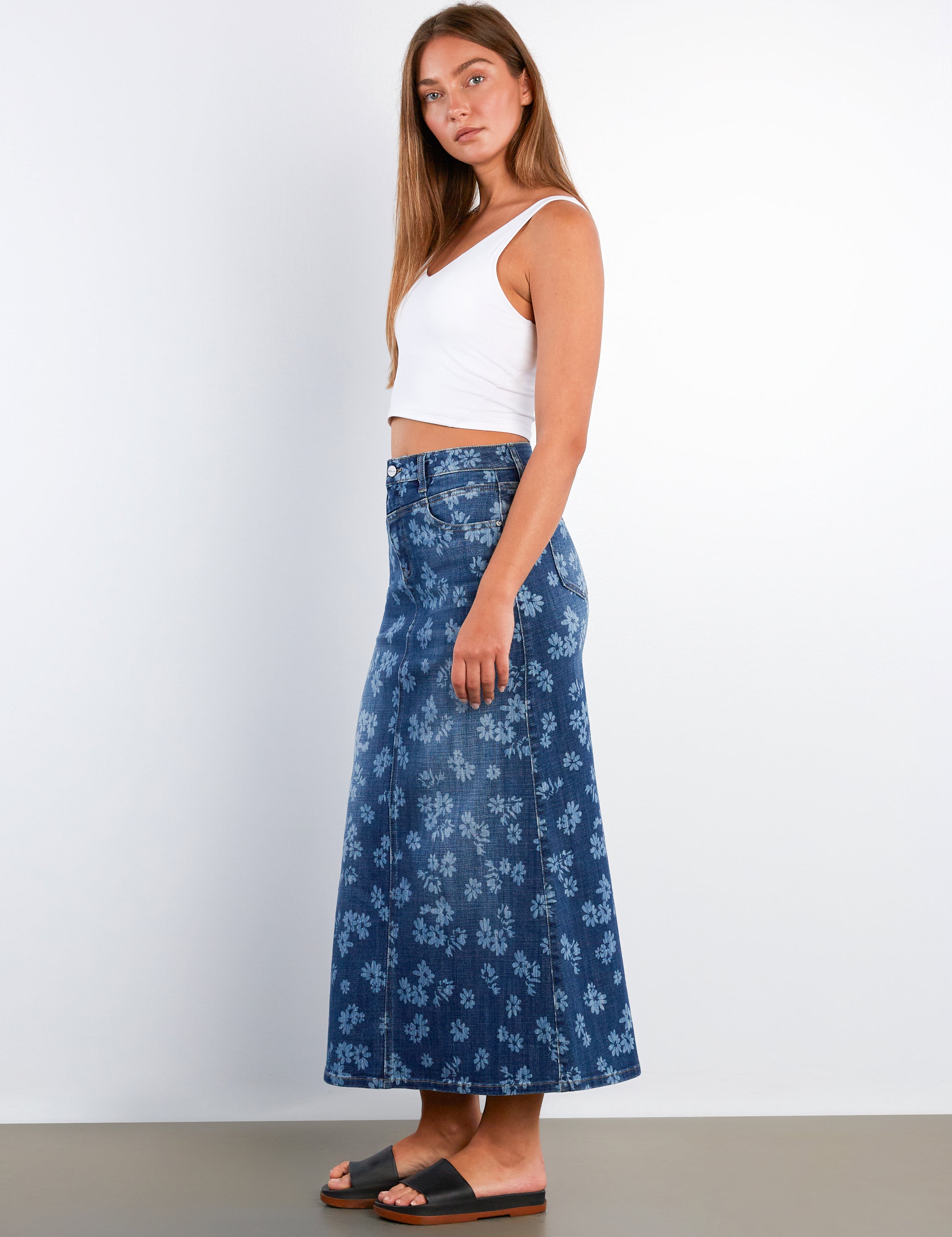 Woman wearing a white top and blue floral skirt against a plain background