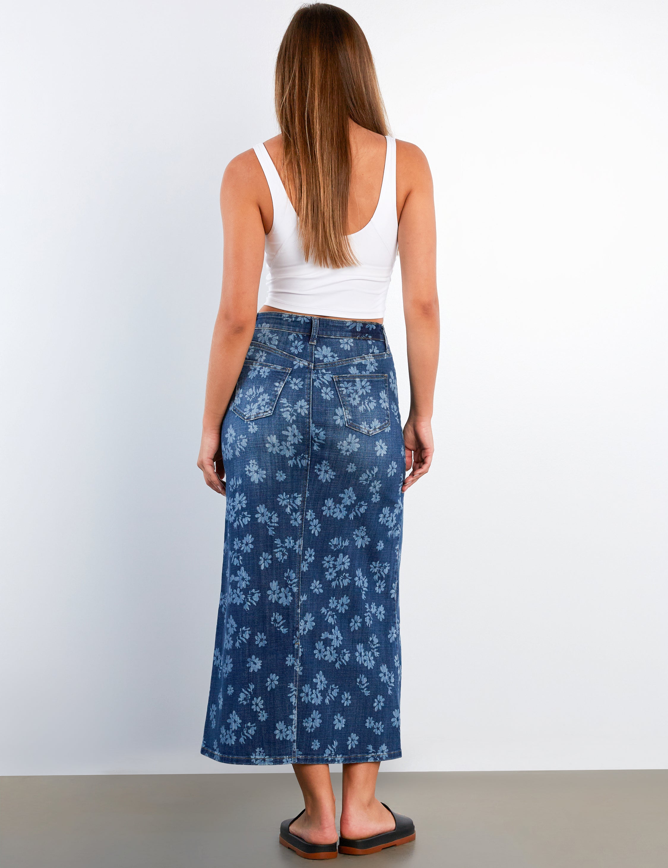 Woman wearing a white tank top and blue floral skirt on a plain background