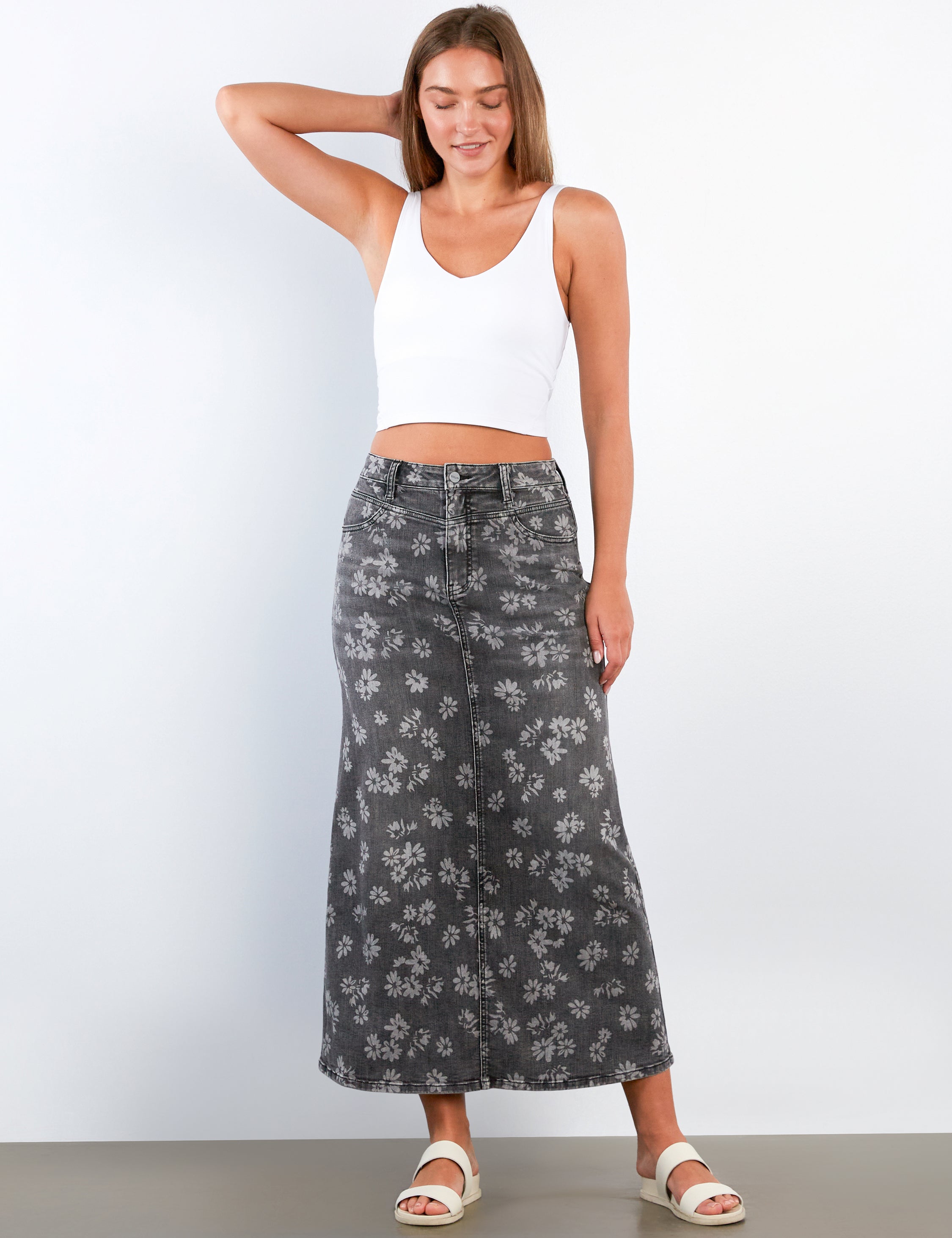 Woman wearing a white tank top and gray floral skirt against a white background
