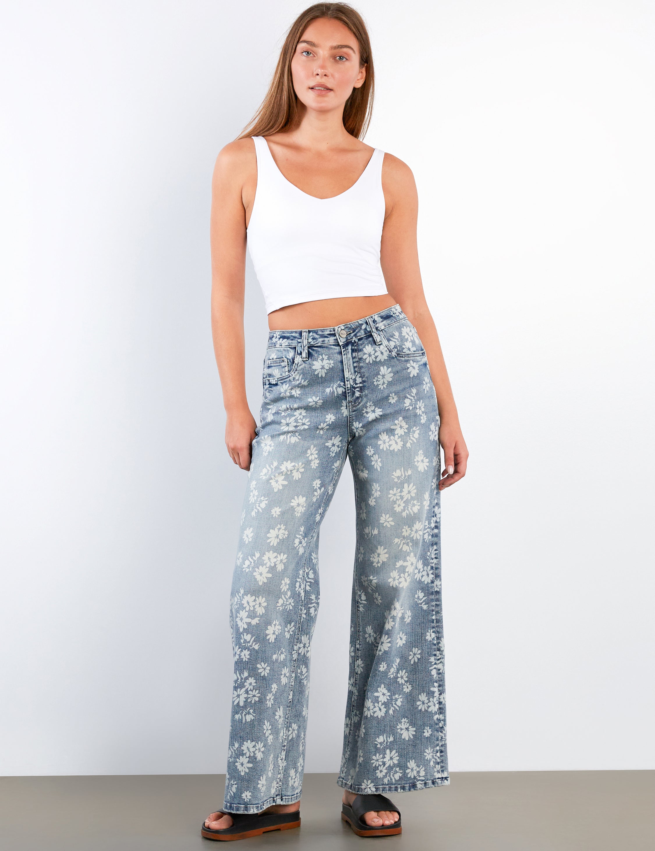 Woman wearing a white tank top and blue floral pants against a white background