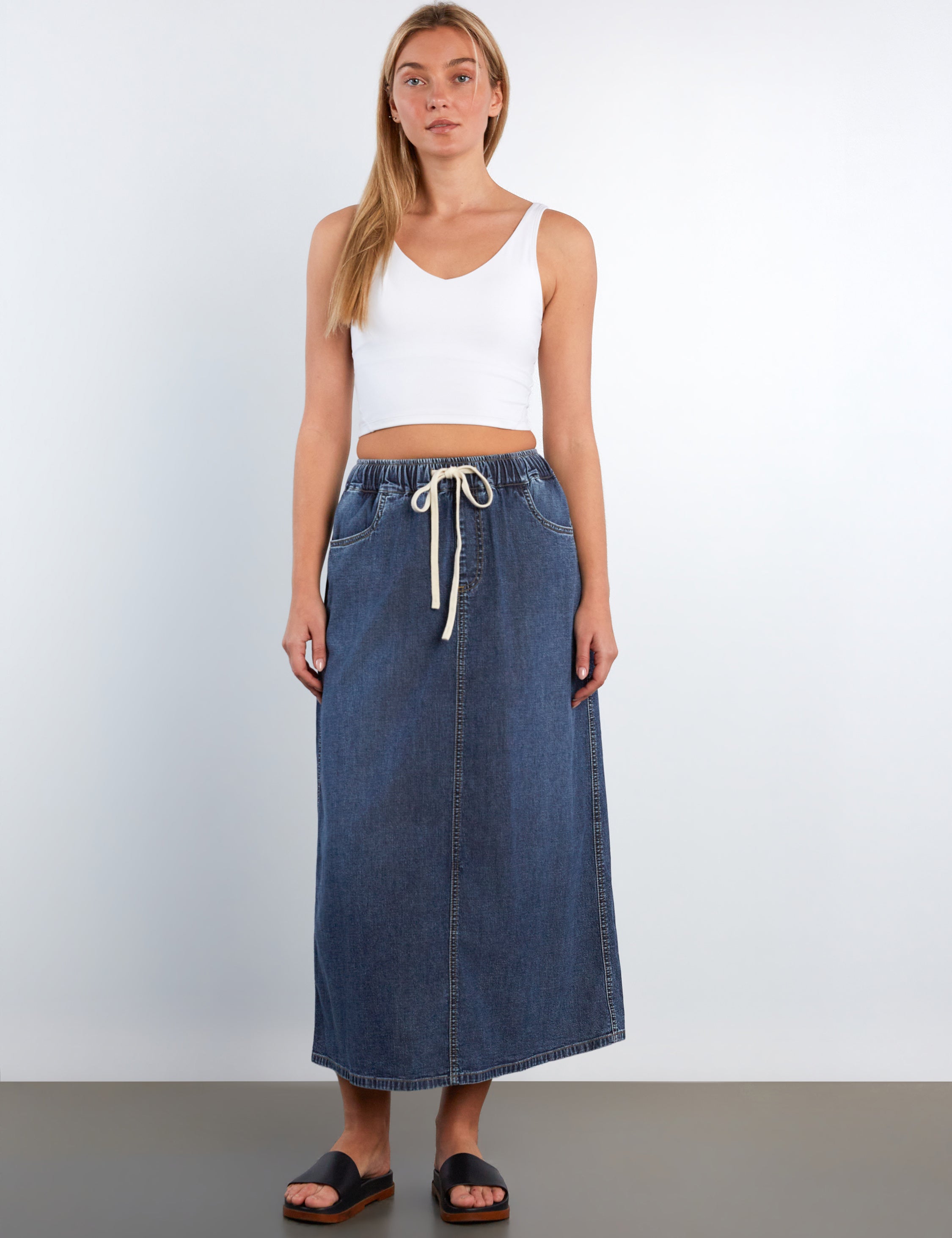 Woman wearing a white tank top and blue denim skirt on a plain background
