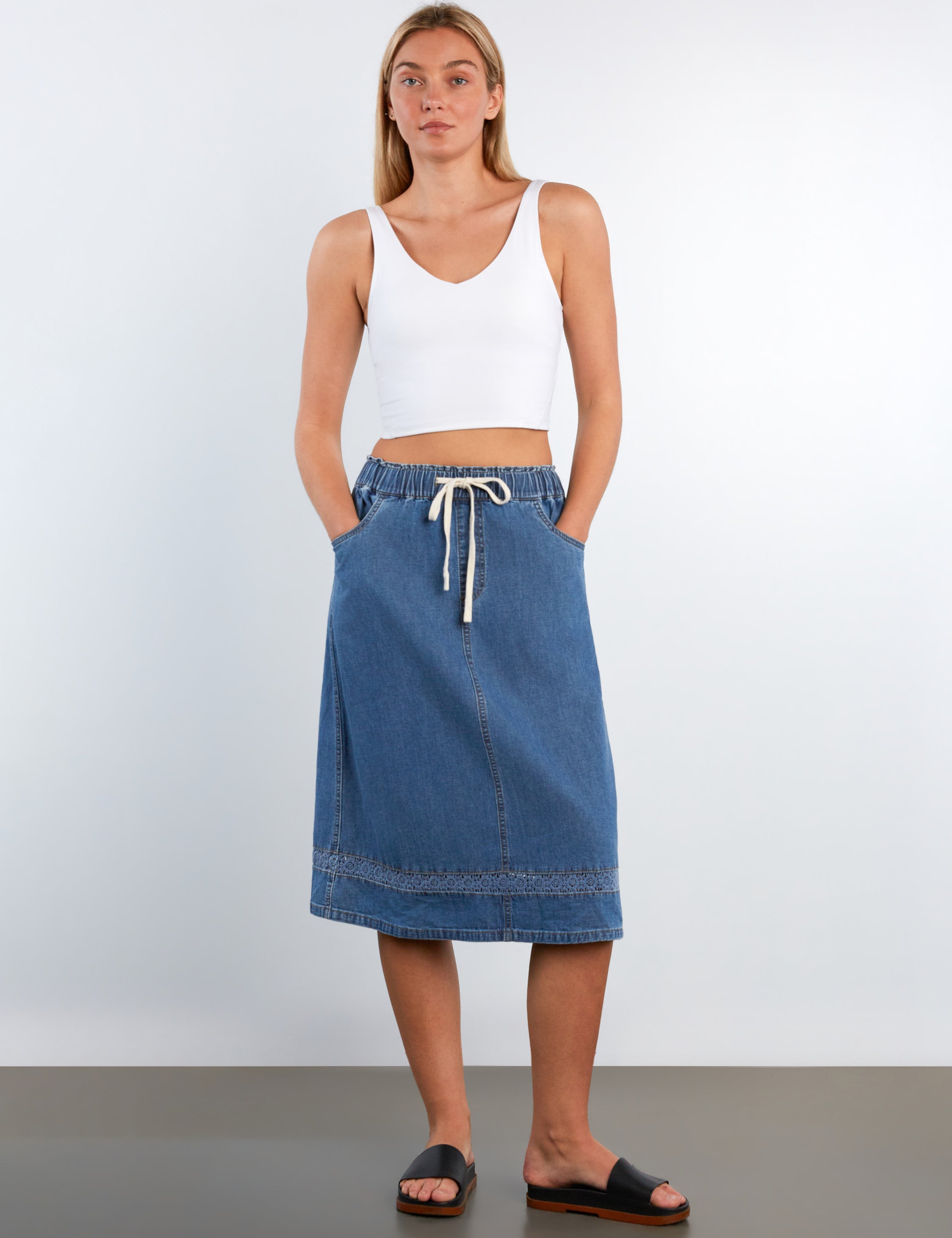 Woman wearing a white tank top and blue denim skirt on a plain background