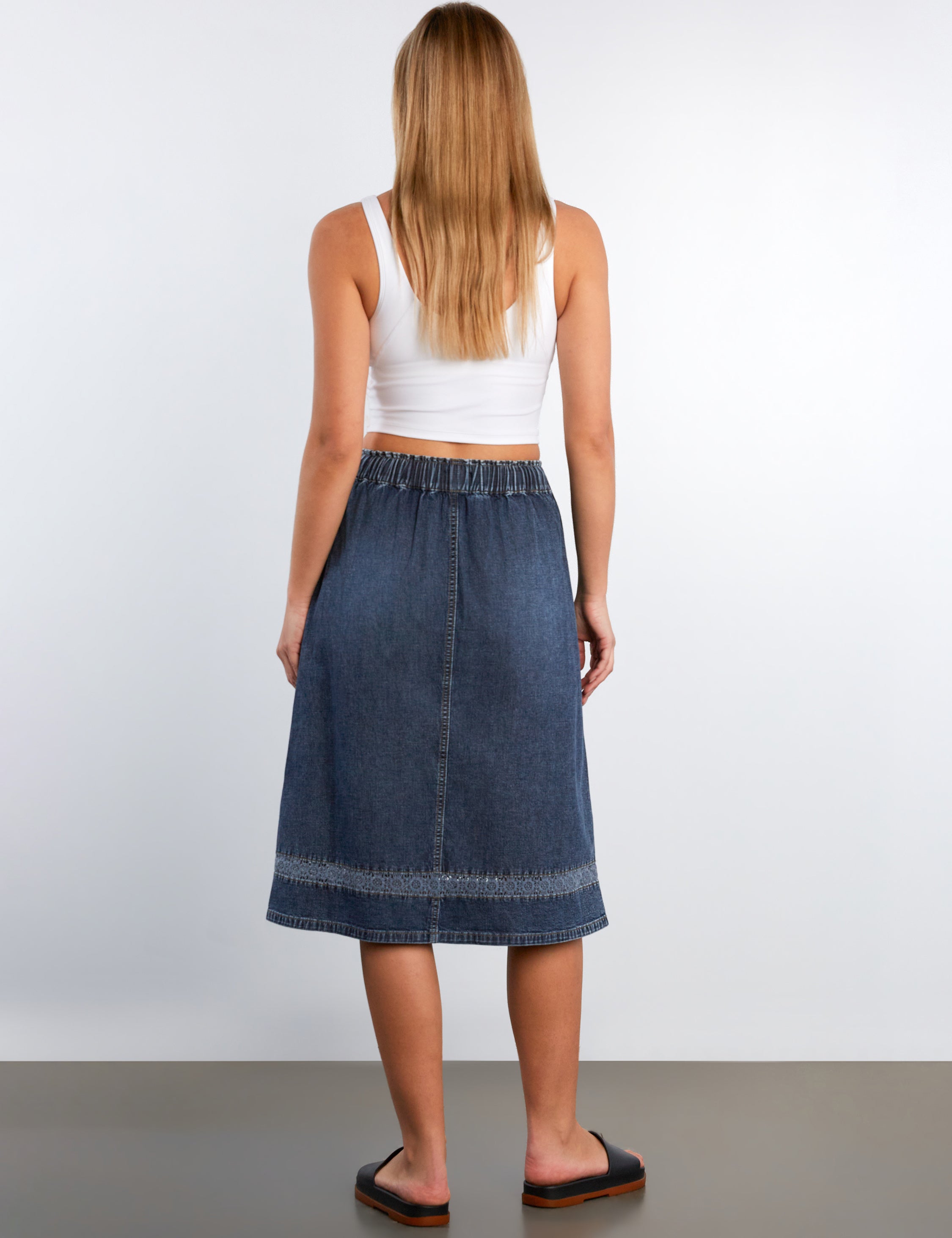 Woman wearing a blue denim skirt and white top on a plain background