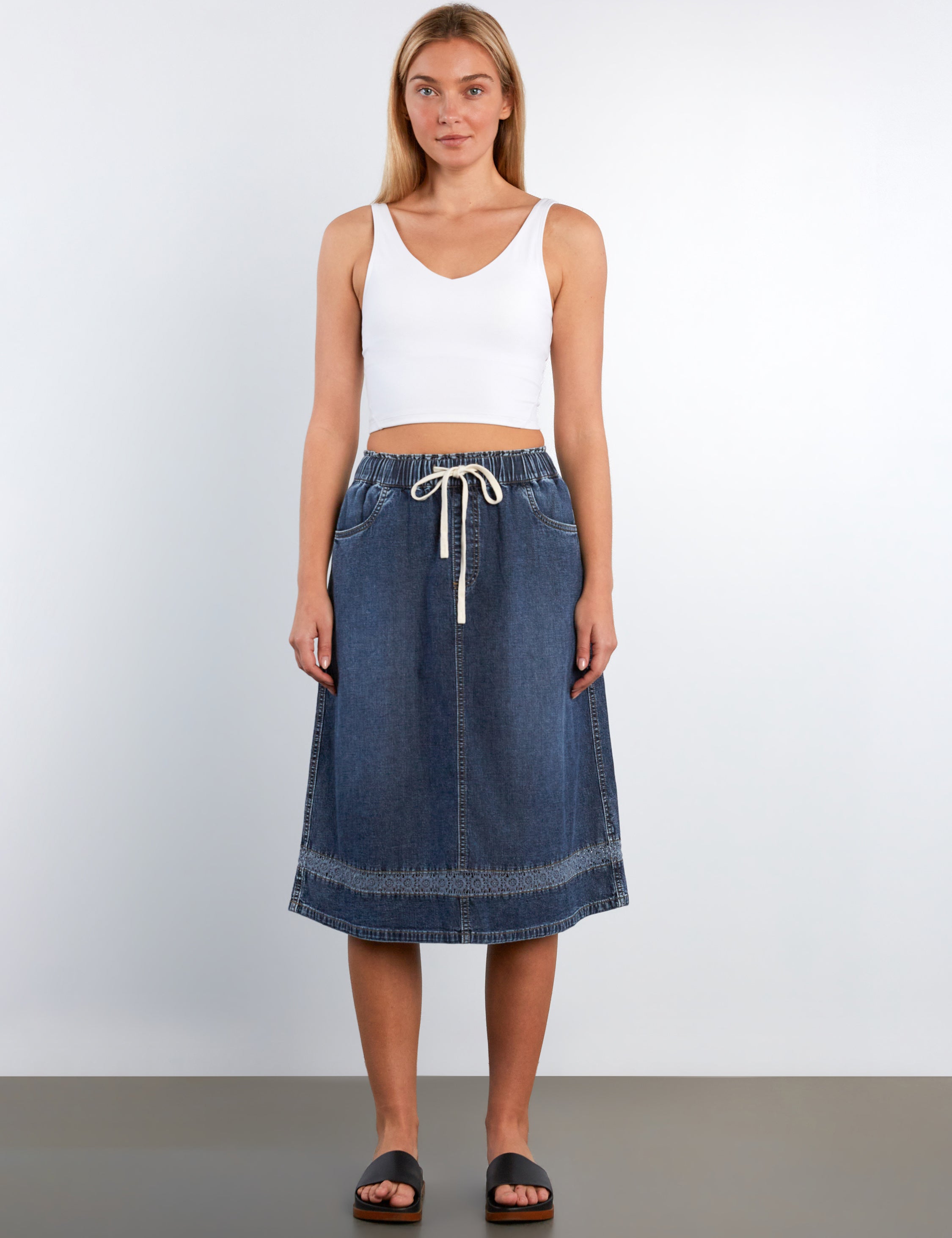 Woman wearing a white tank top and blue denim skirt on a plain background