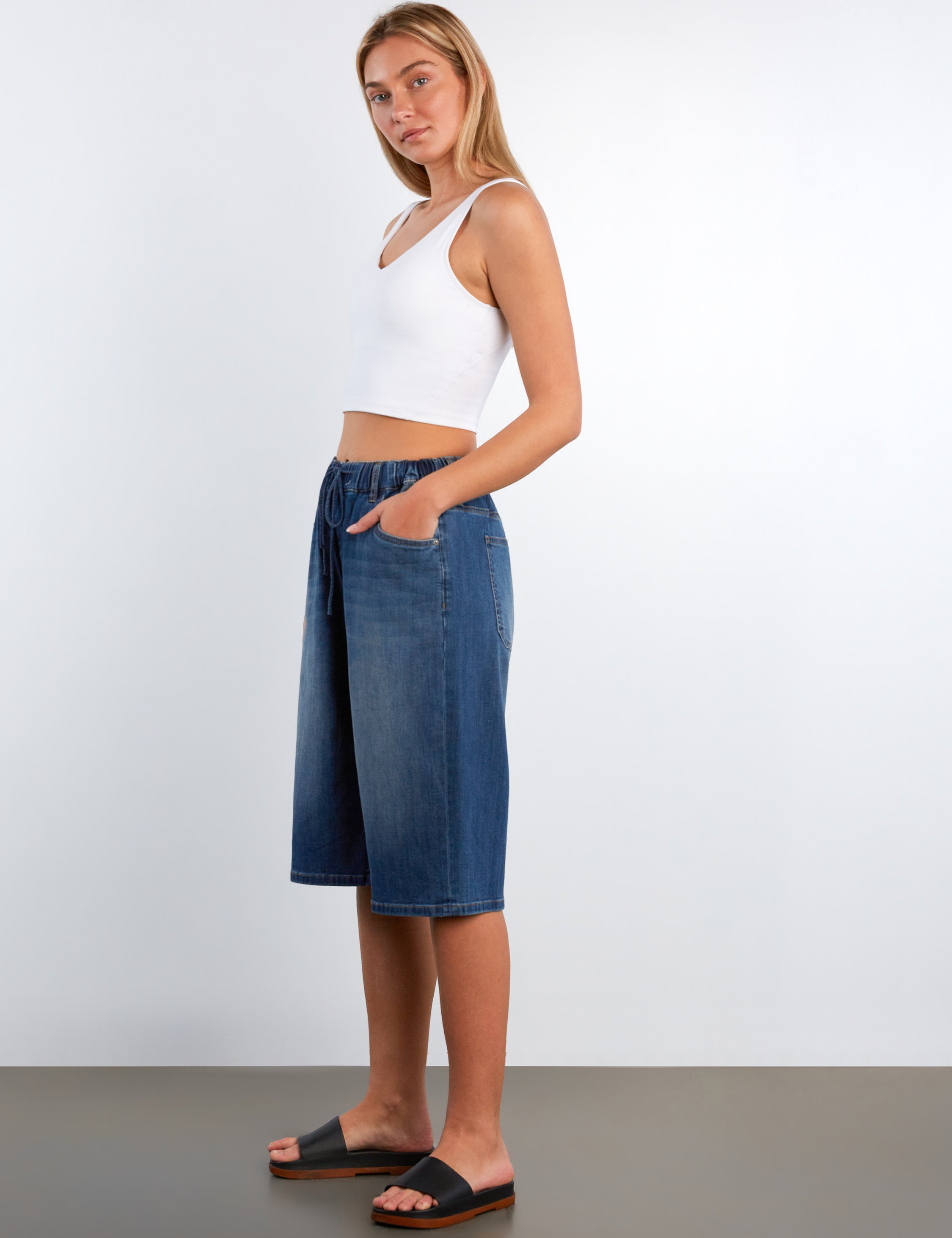 Woman wearing a white top and blue denim skirt against a plain background