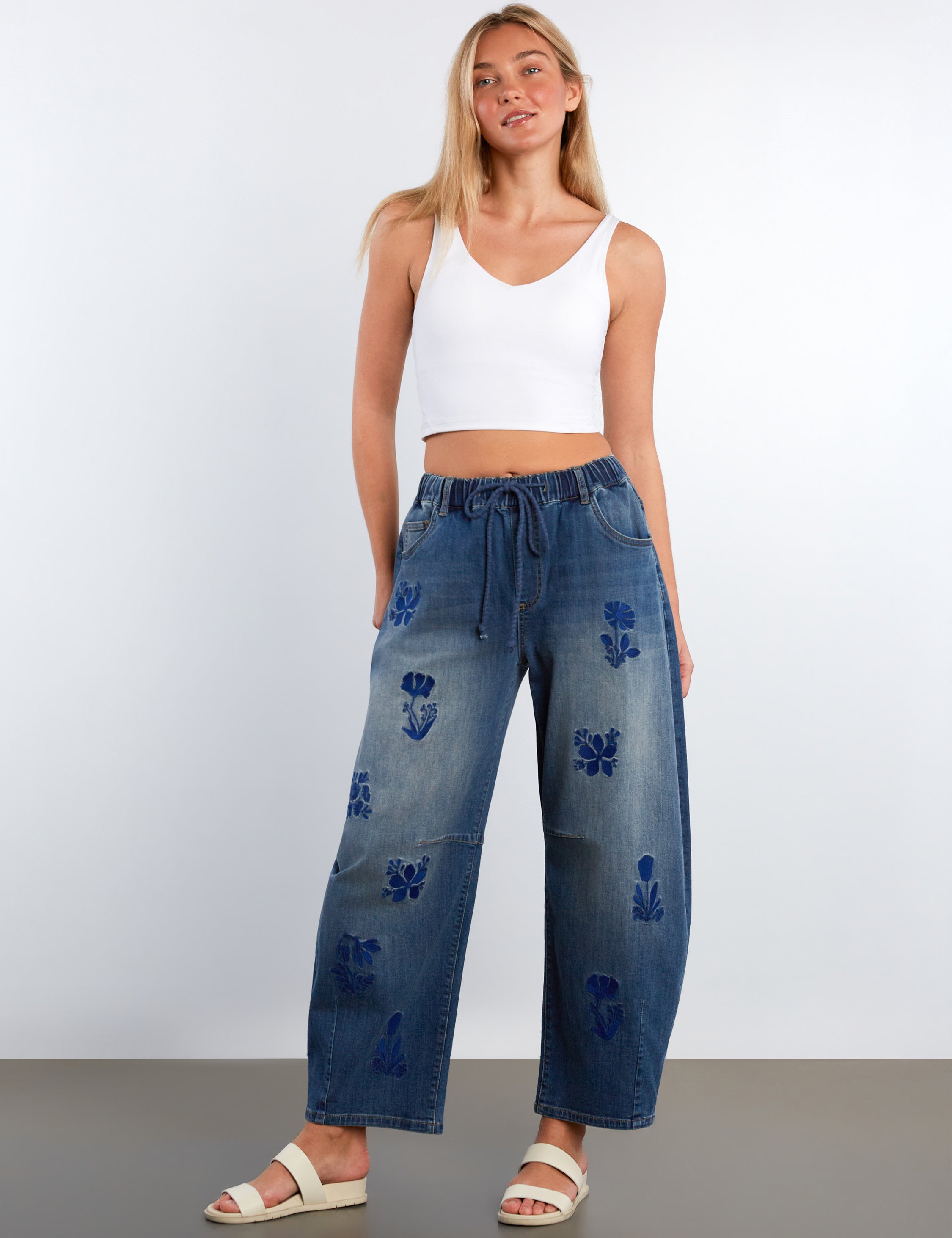 Woman wearing blue denim pants with floral embroidery on a white background