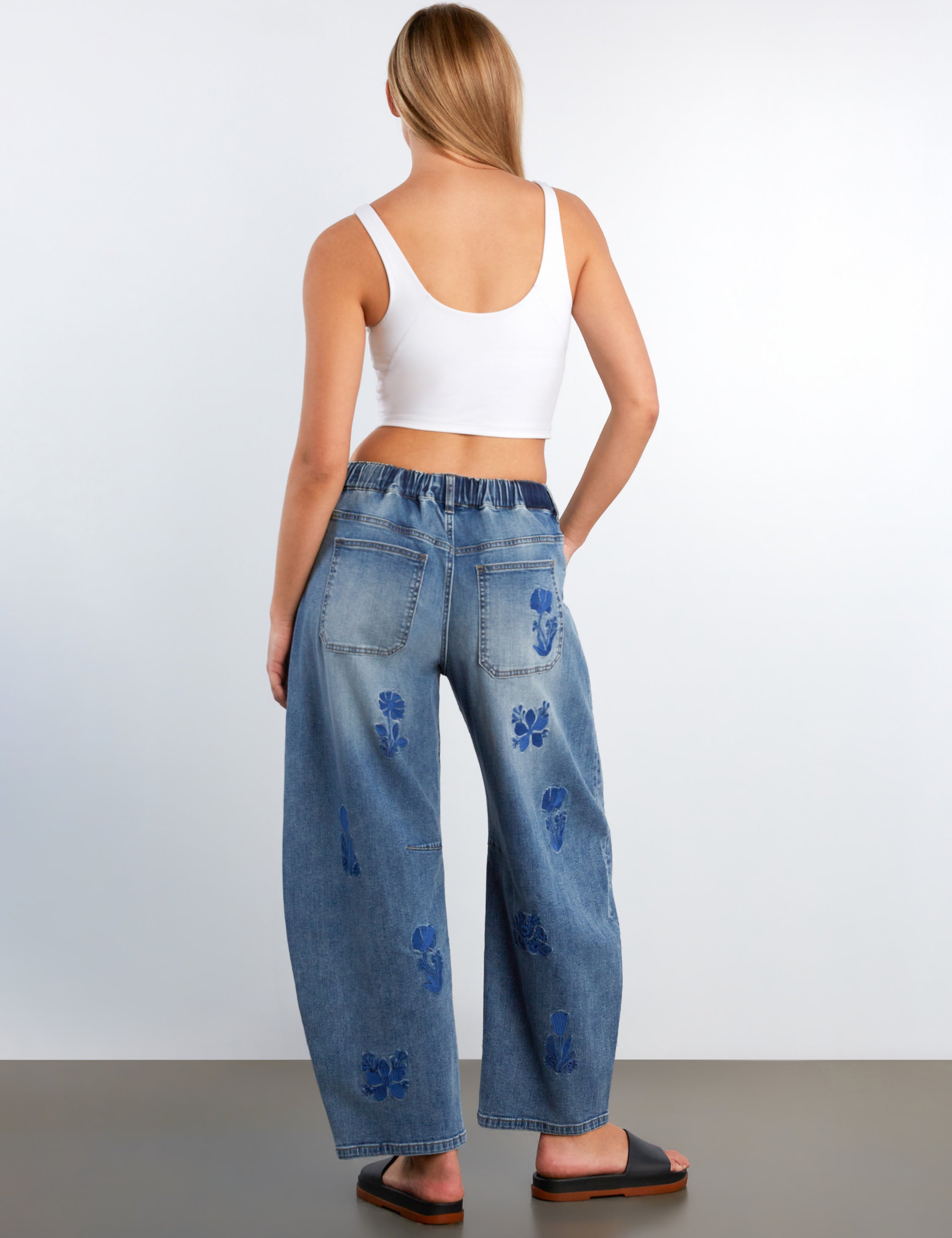 Woman wearing blue jeans with floral patterns on a plain background