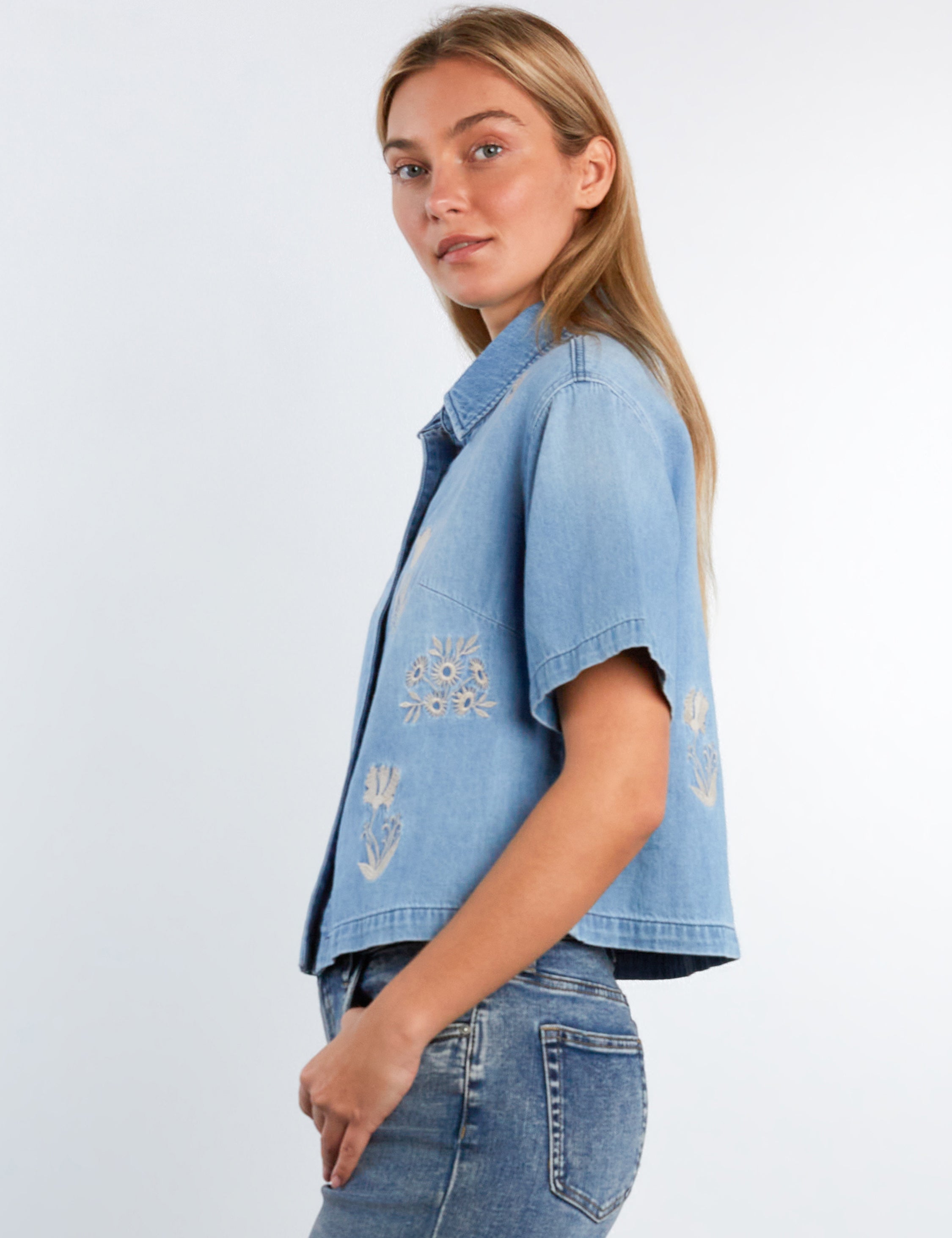 Woman wearing a denim jacket with floral embroidery on a white background