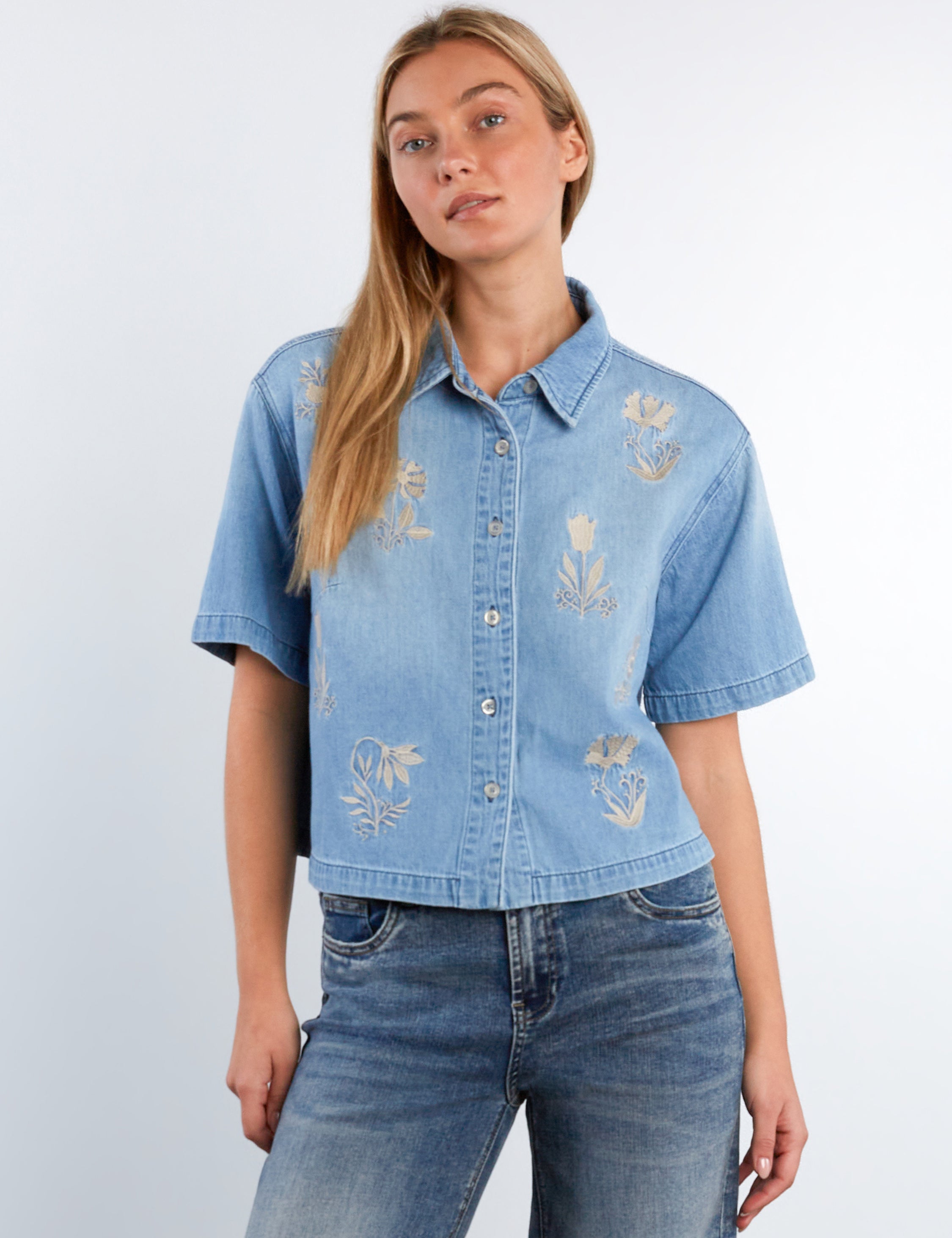 Woman wearing a light blue denim shirt with floral embroidery on a white background