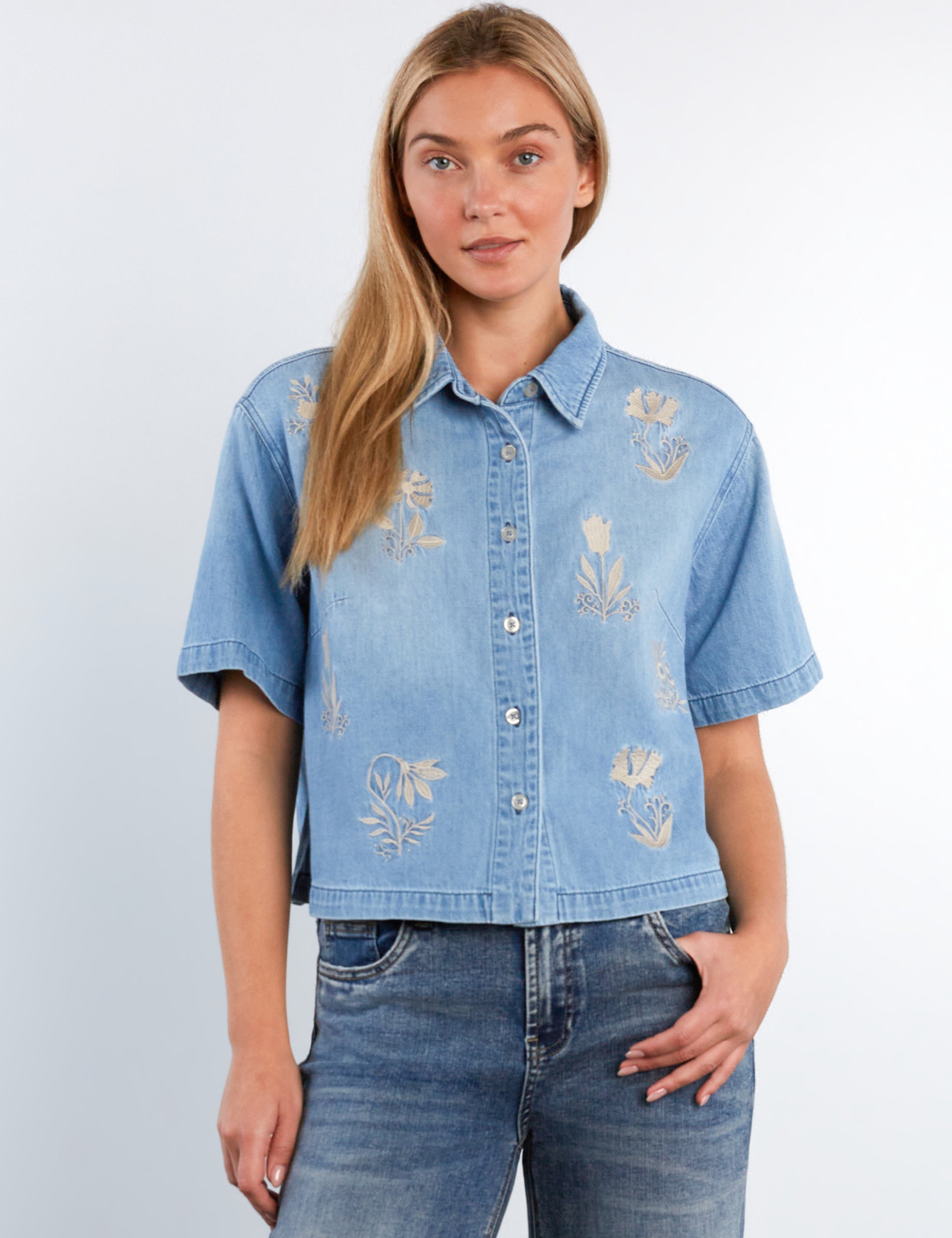 Woman wearing a denim shirt with floral embroidery against a light gray background