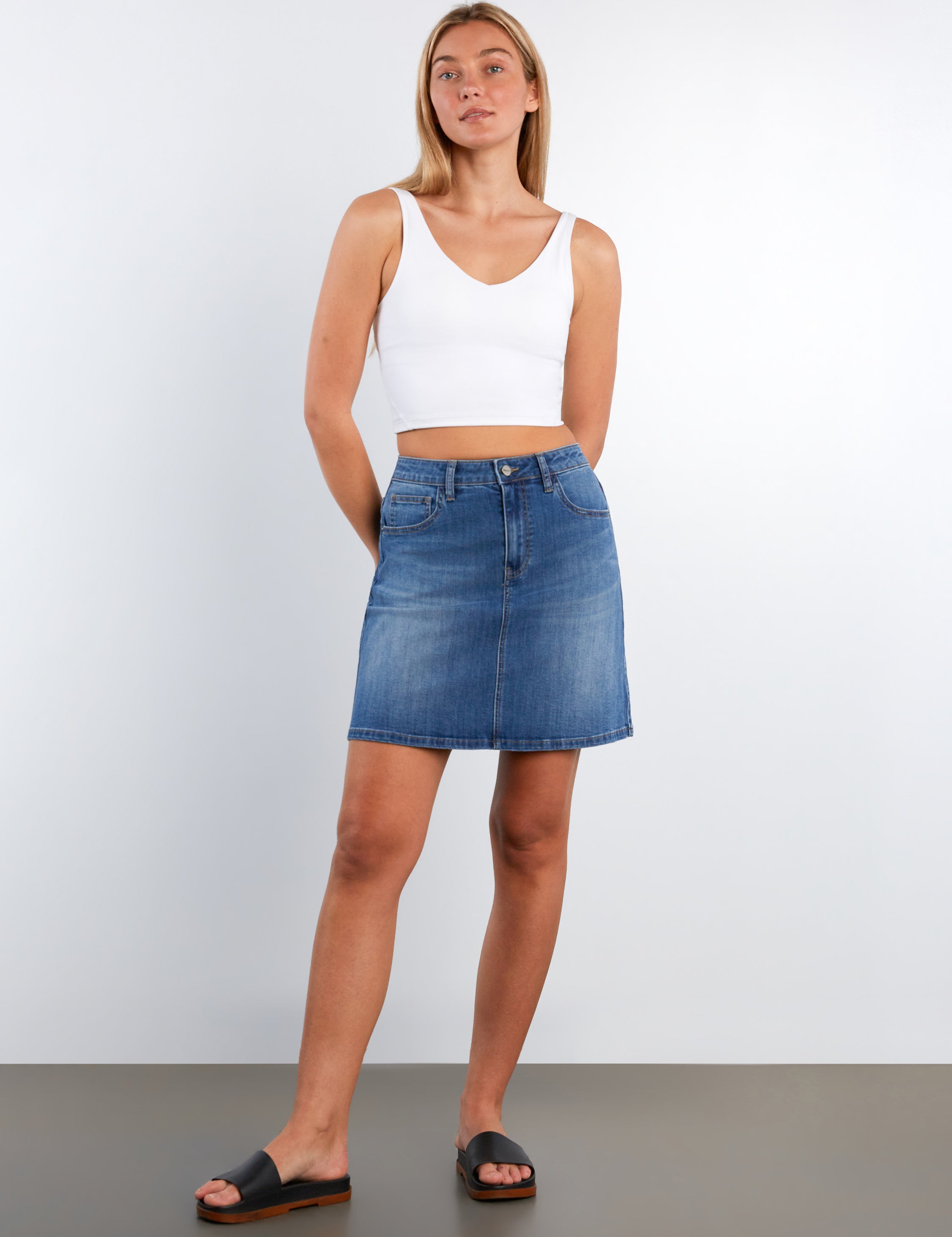 Woman wearing a white tank top and blue denim skirt on a plain background