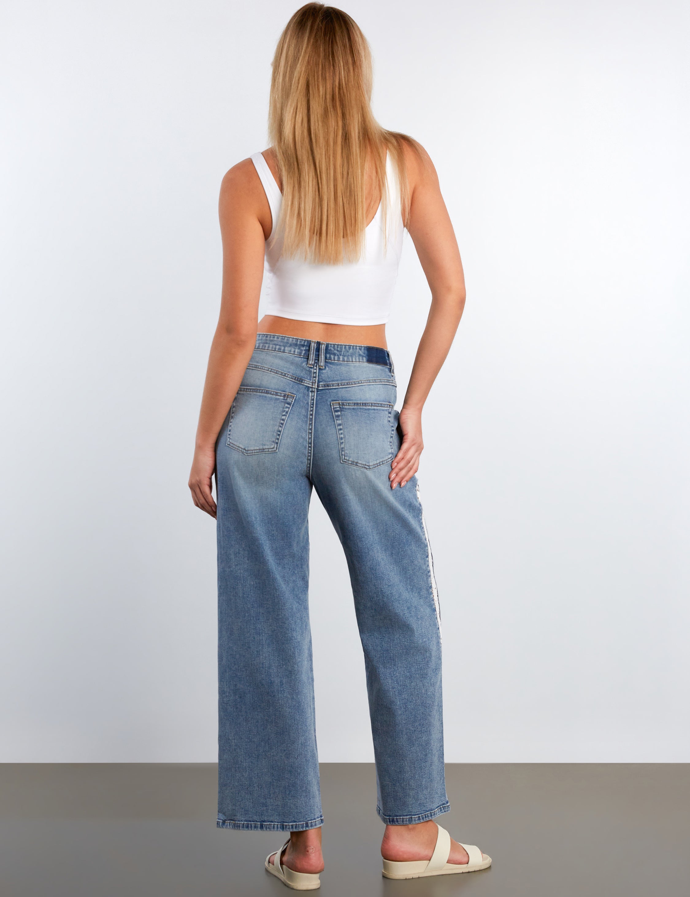 Woman wearing blue jeans and a white top on a plain background