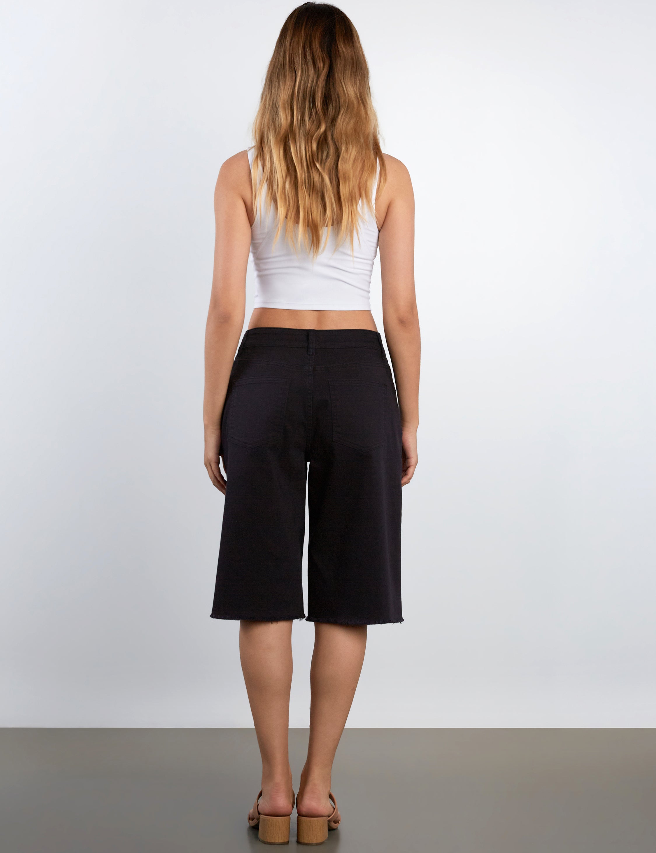 Woman wearing a white crop top and black shorts on a plain background