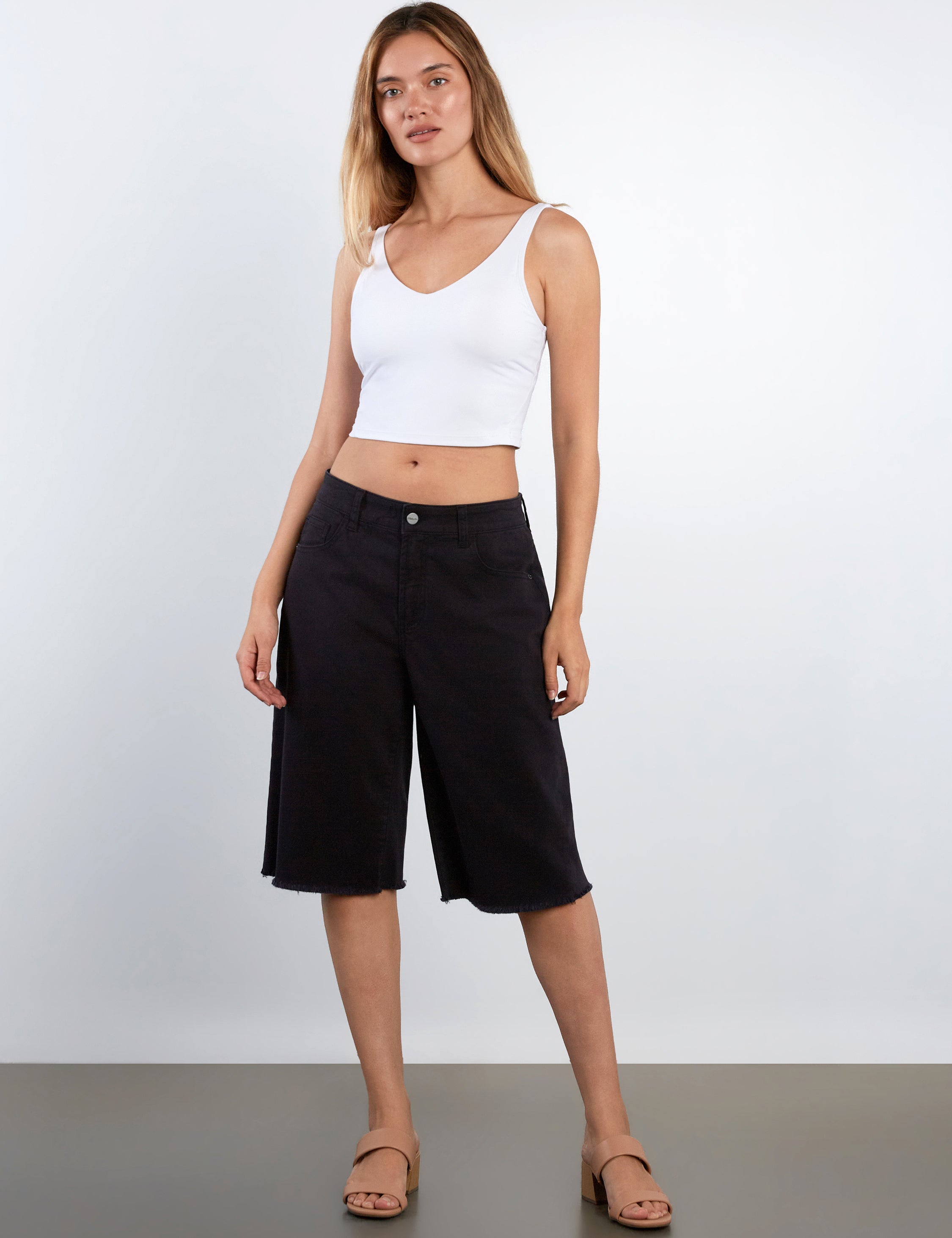 Woman wearing a white tank top and black shorts against a plain background